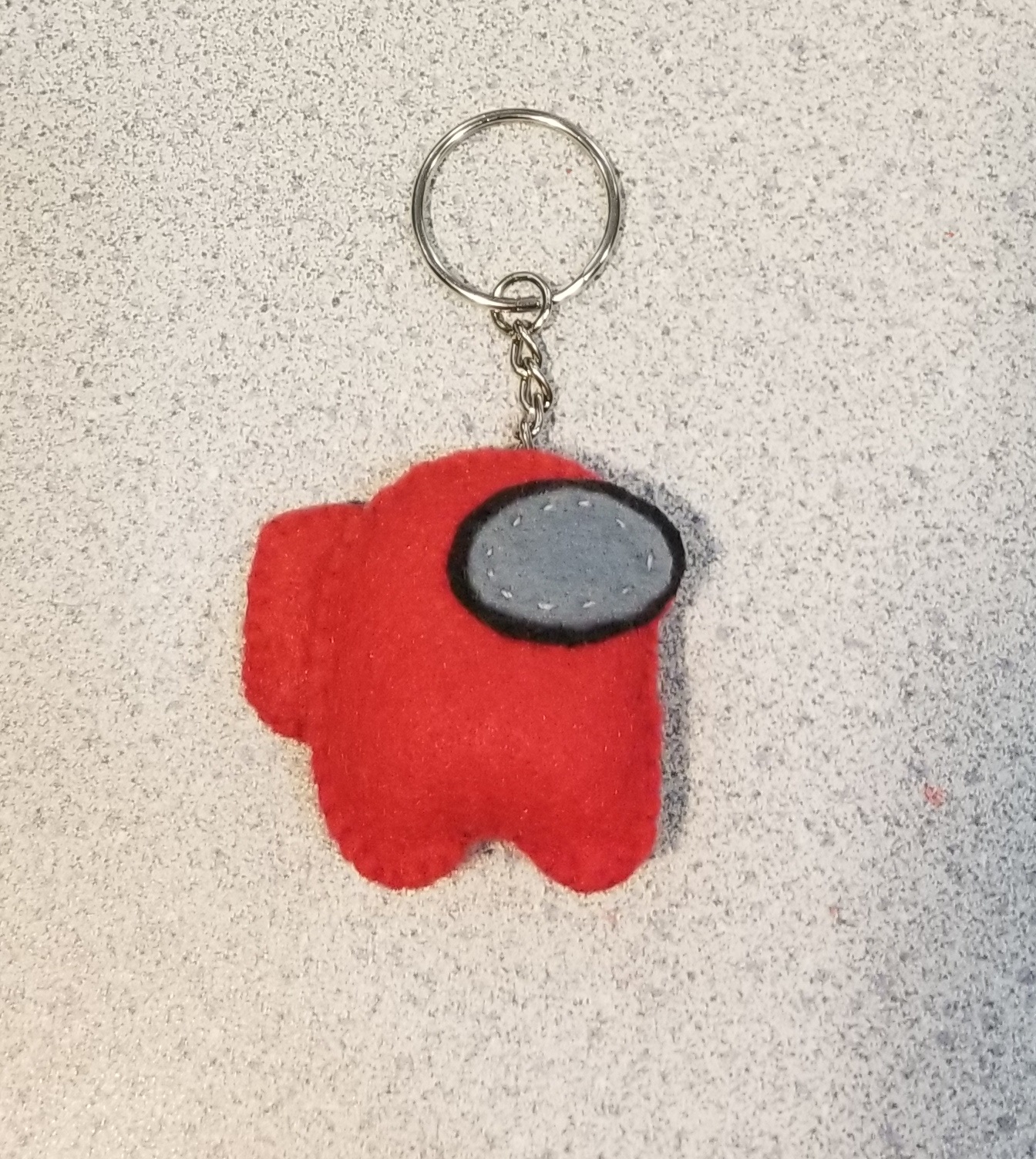 A red felt keychain of a crewmate character from the video game Among Us