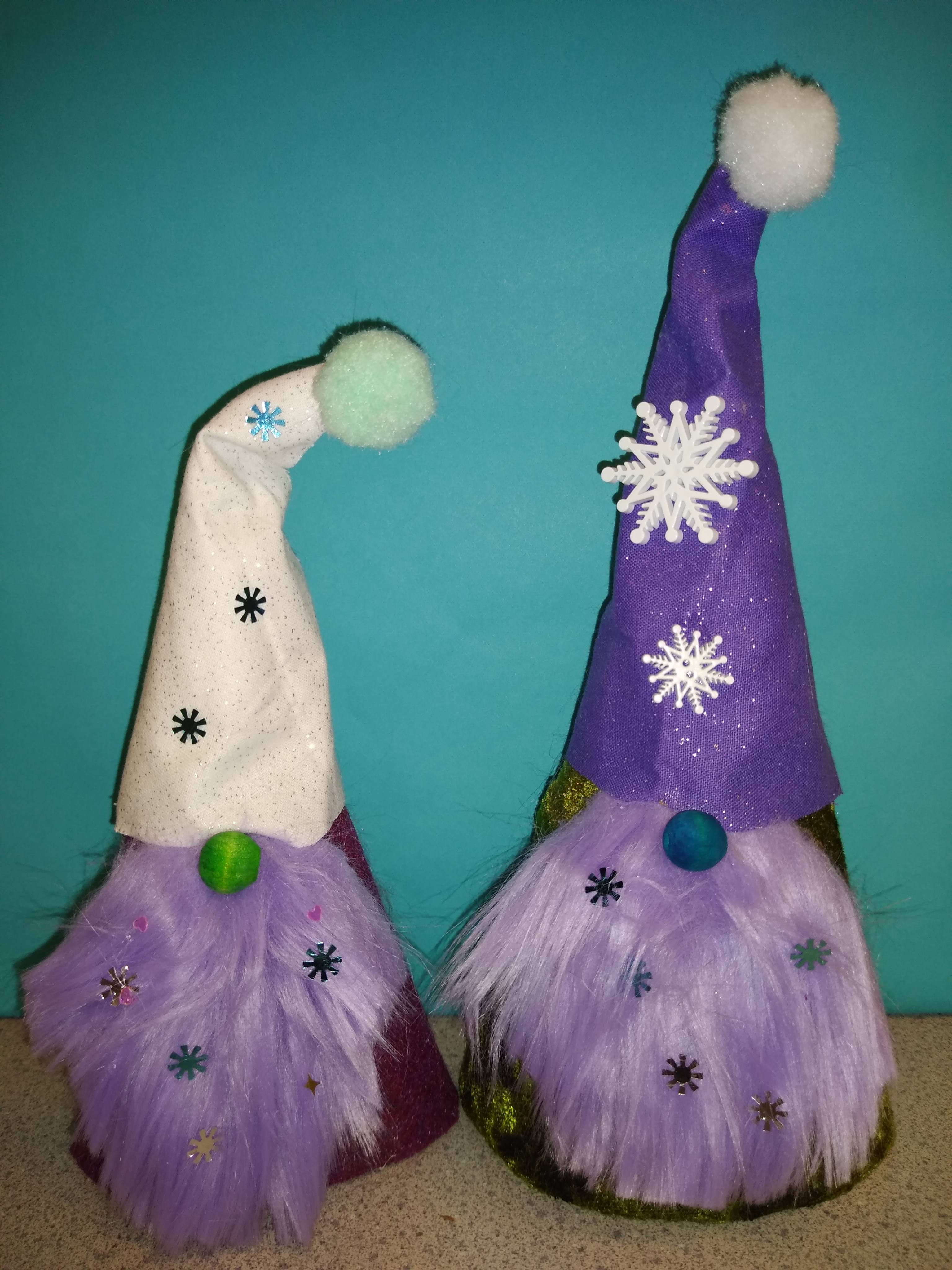 Two gnomes made out of felt and fake fur, decorated in a winter theme.
