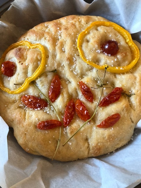 A round loaf of bread with a depiction of flowers made out of tomatoes, bell peppers, and fresh herbs
