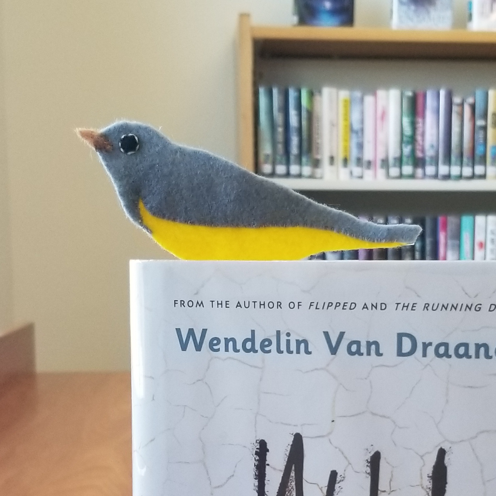 A gray and yellow felt bird bookmark sticking out of the top of the book. The bird is visible in profile and is a Connecticut Warbler.