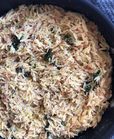 A pan of cheesy broccoli orzo: off white pasta with visible cheese and pepper with deep green pieces of broccoli throughout
