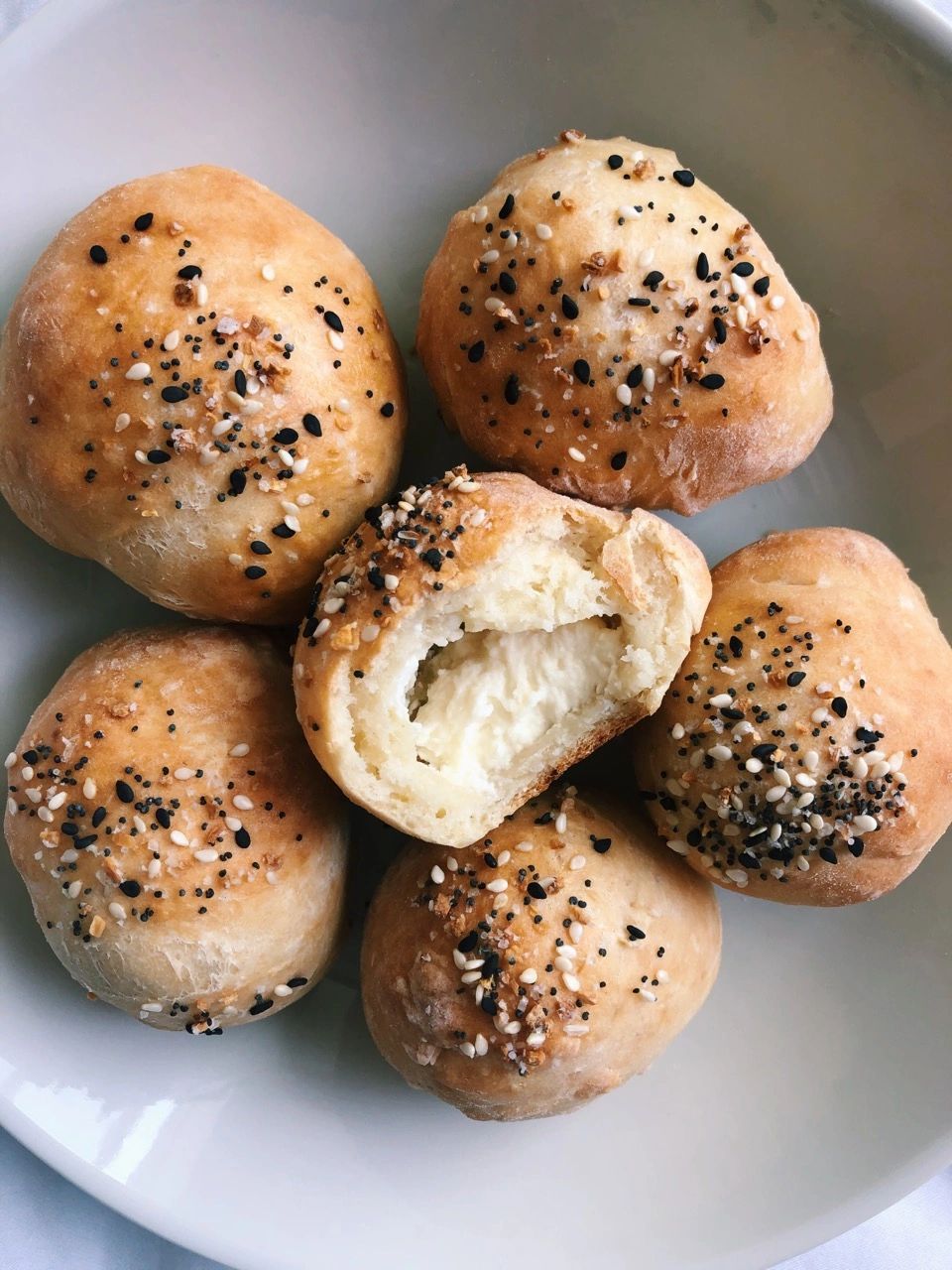 Six small bagel balls with everything seasoning; the center has a bite taken out of it, exposing its cream cheese filling