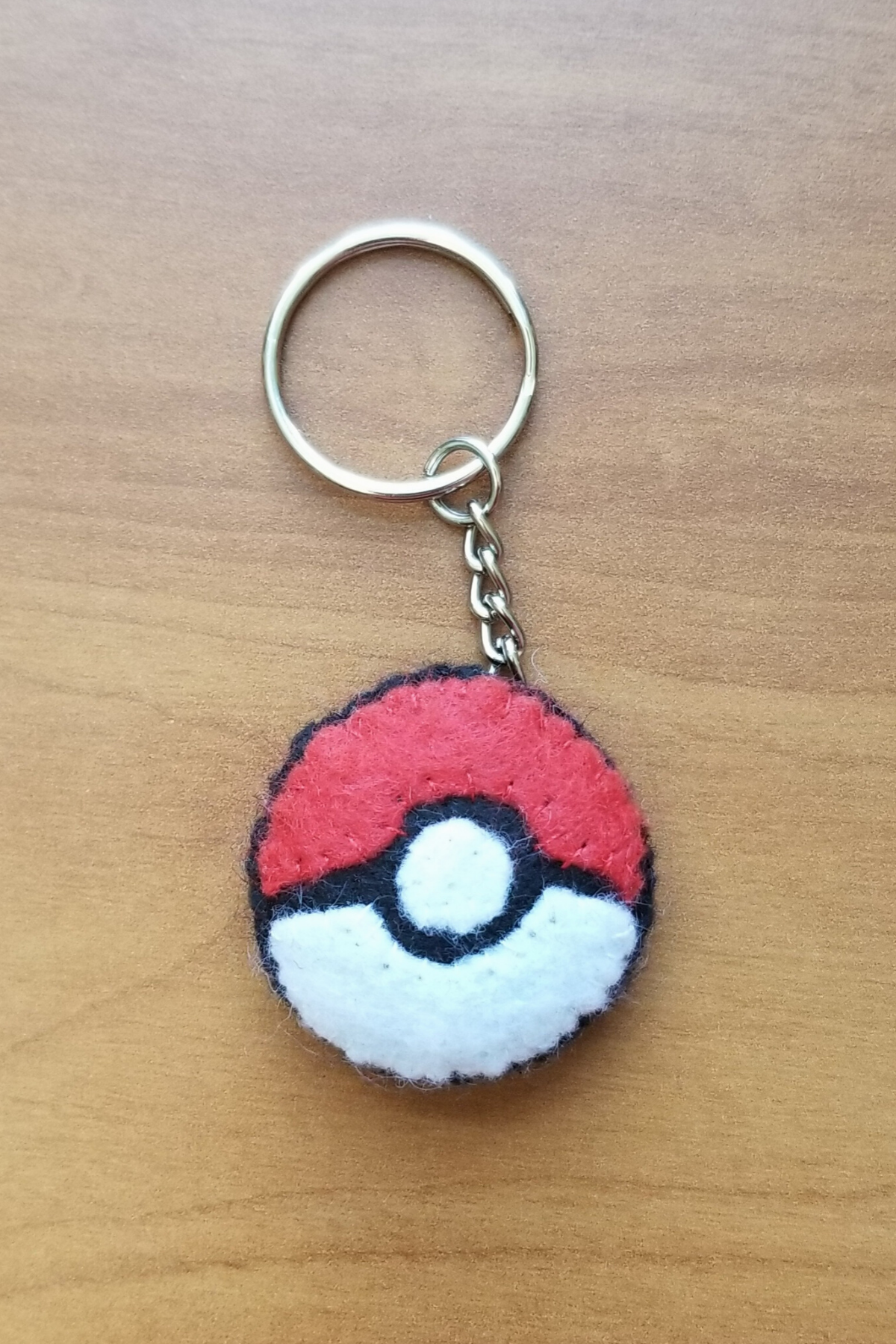 A keychain with a round disc of black, red, and white that is sewn together to look like a Pokeball from Pokemon
