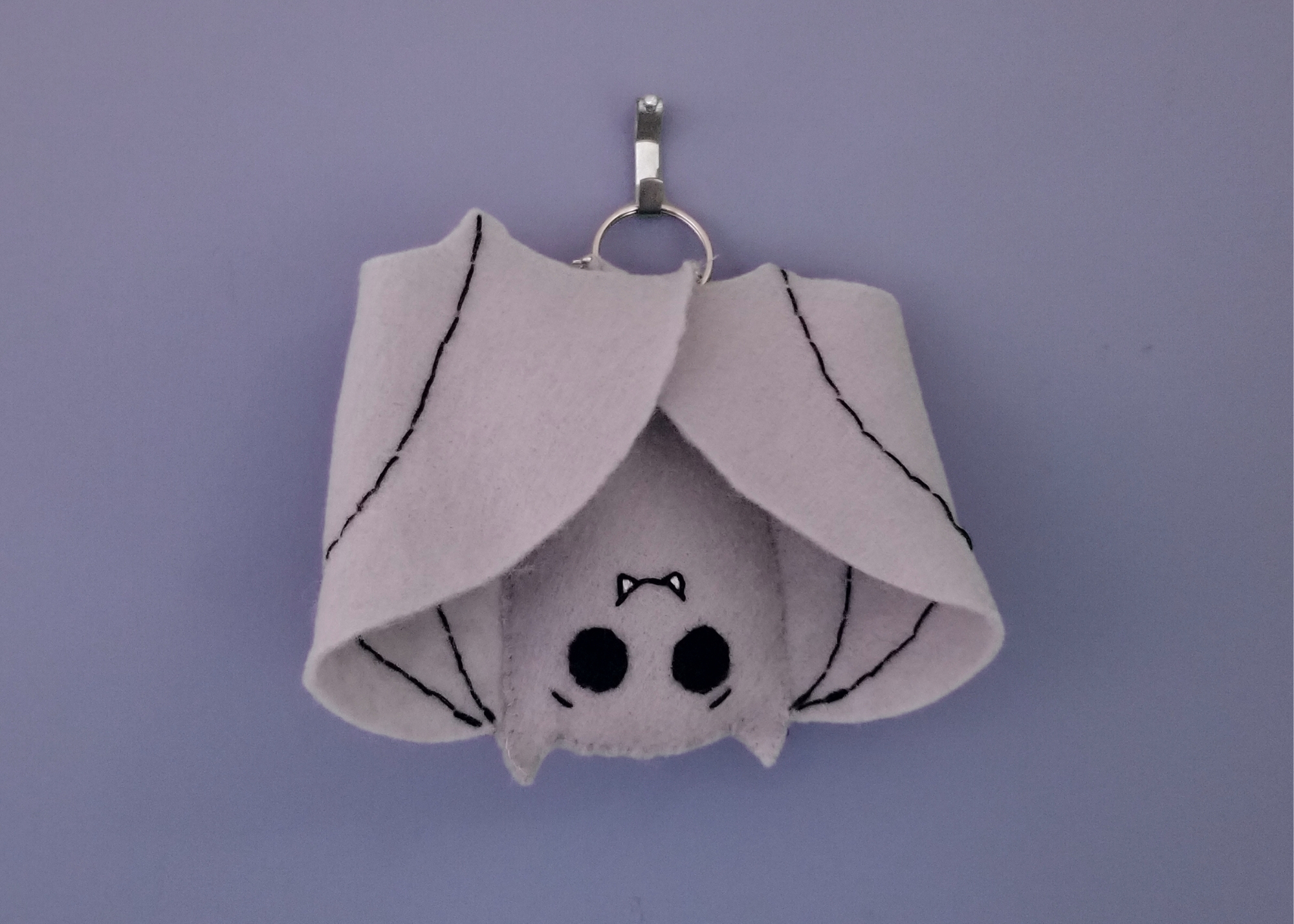 A gray felt bat plush with a little smiling face hanging upside down