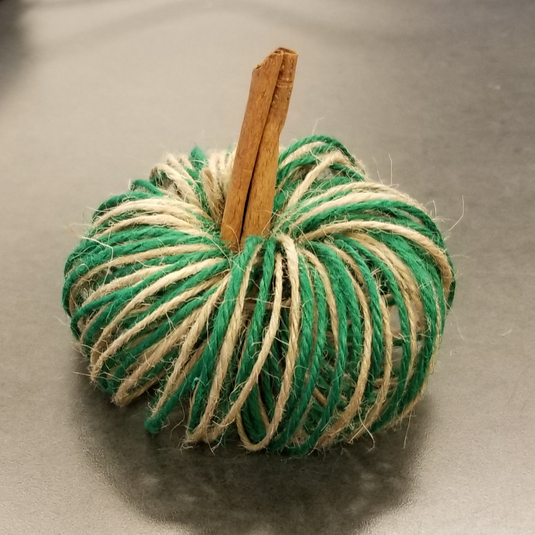 A pumpkin made of green and tan twine wrapped in a coil with a cinnamon stick stem