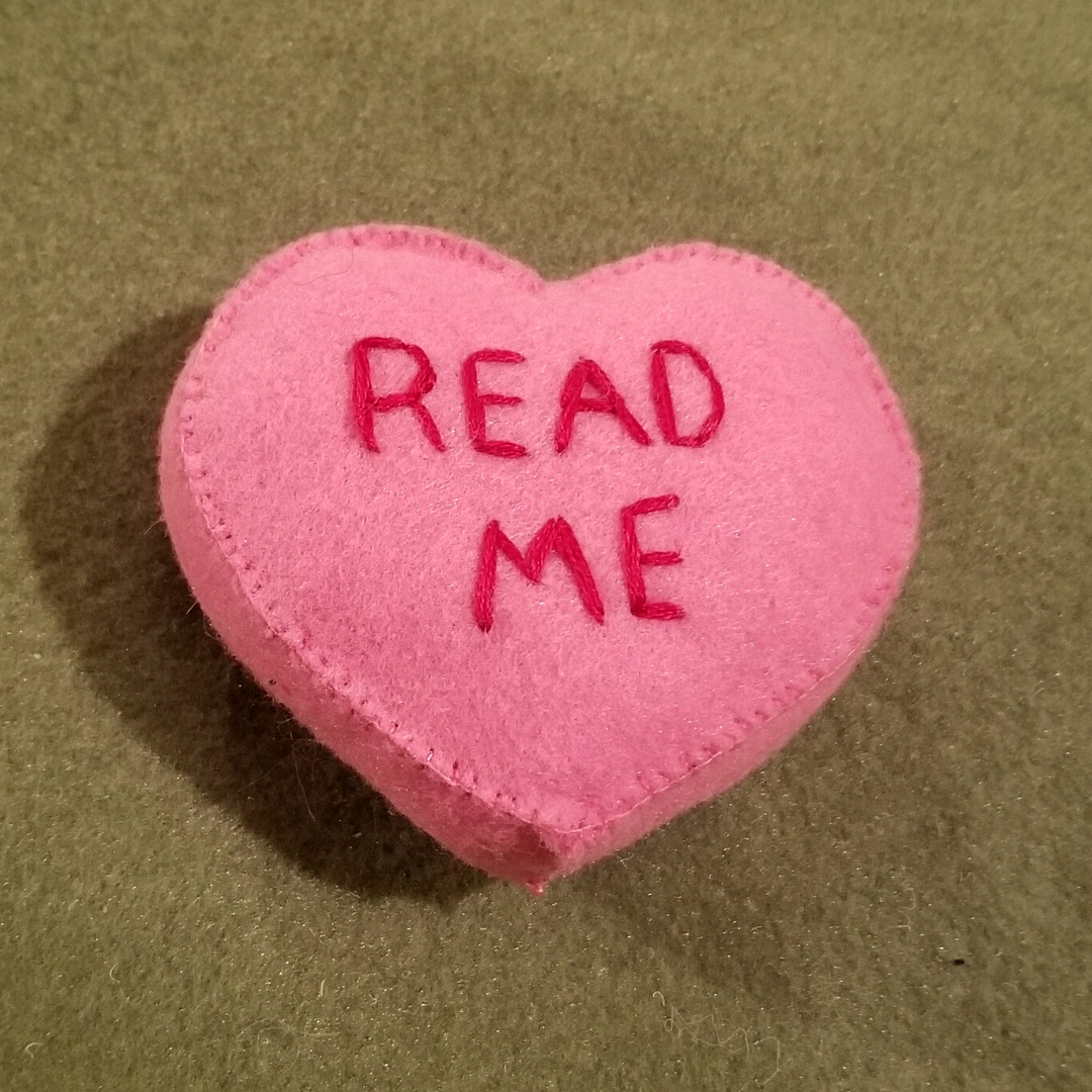 A pink felt conversation heart with the words "Read Me" embroidered on the front