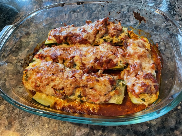 Zucchini lasagna boats, consisting of zucchinis halved lengthwise and stuffed with lasagna filling. The top is golden brown with tomato sauce and