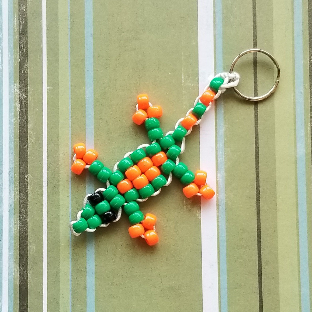 A lizard made of bright green and orange pony beads attached to a metal keychain ring