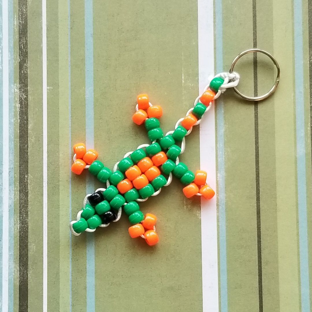 A%20lizard%20made%20of%20bright%20green%20and%20orange%20pony%20beads%20attached%20to%20a%20metal%20keychain%20ring