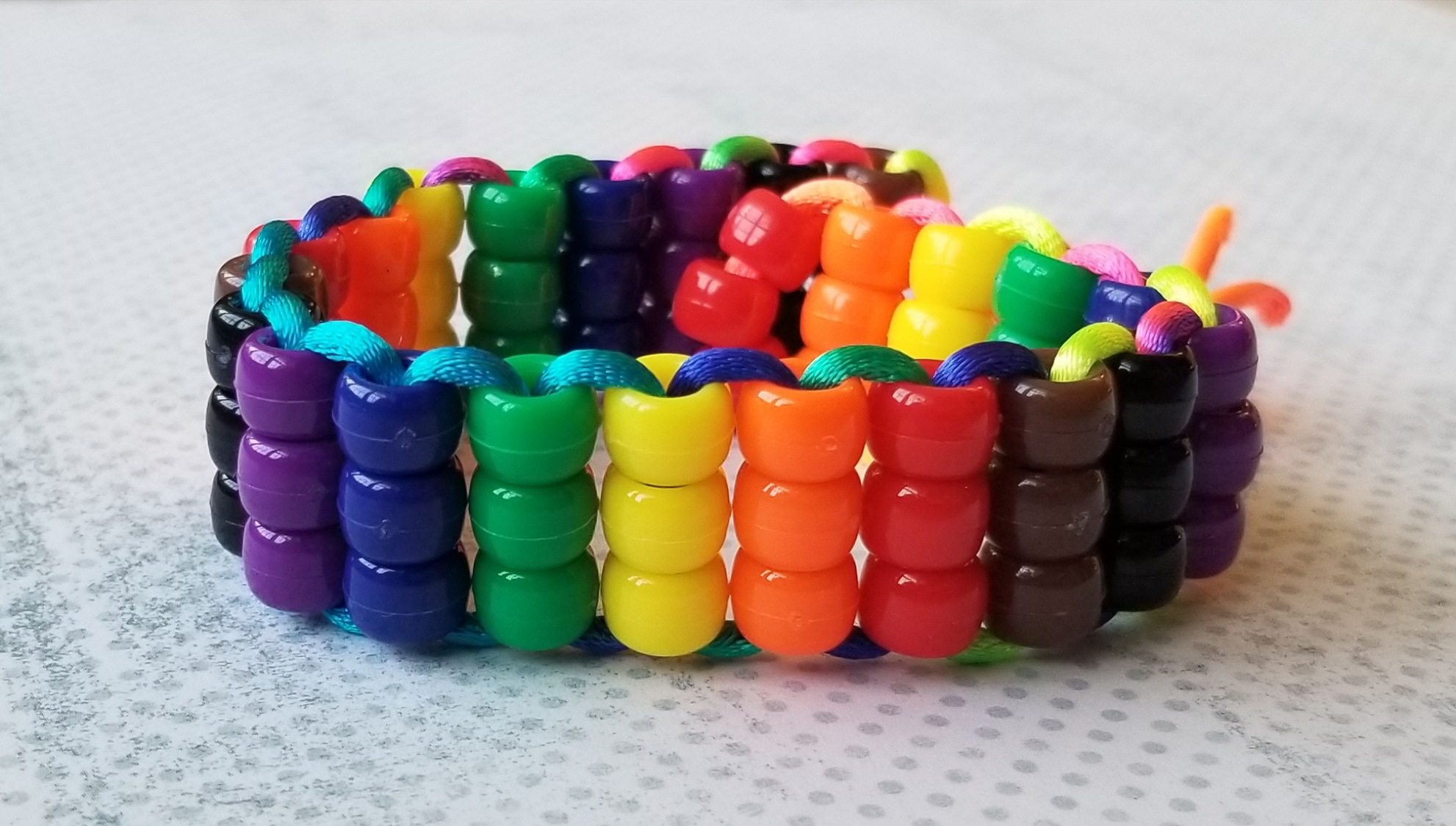 A bracelet made of pony beads in black, brown, red, orange, yellow, green, blue, and purple beads