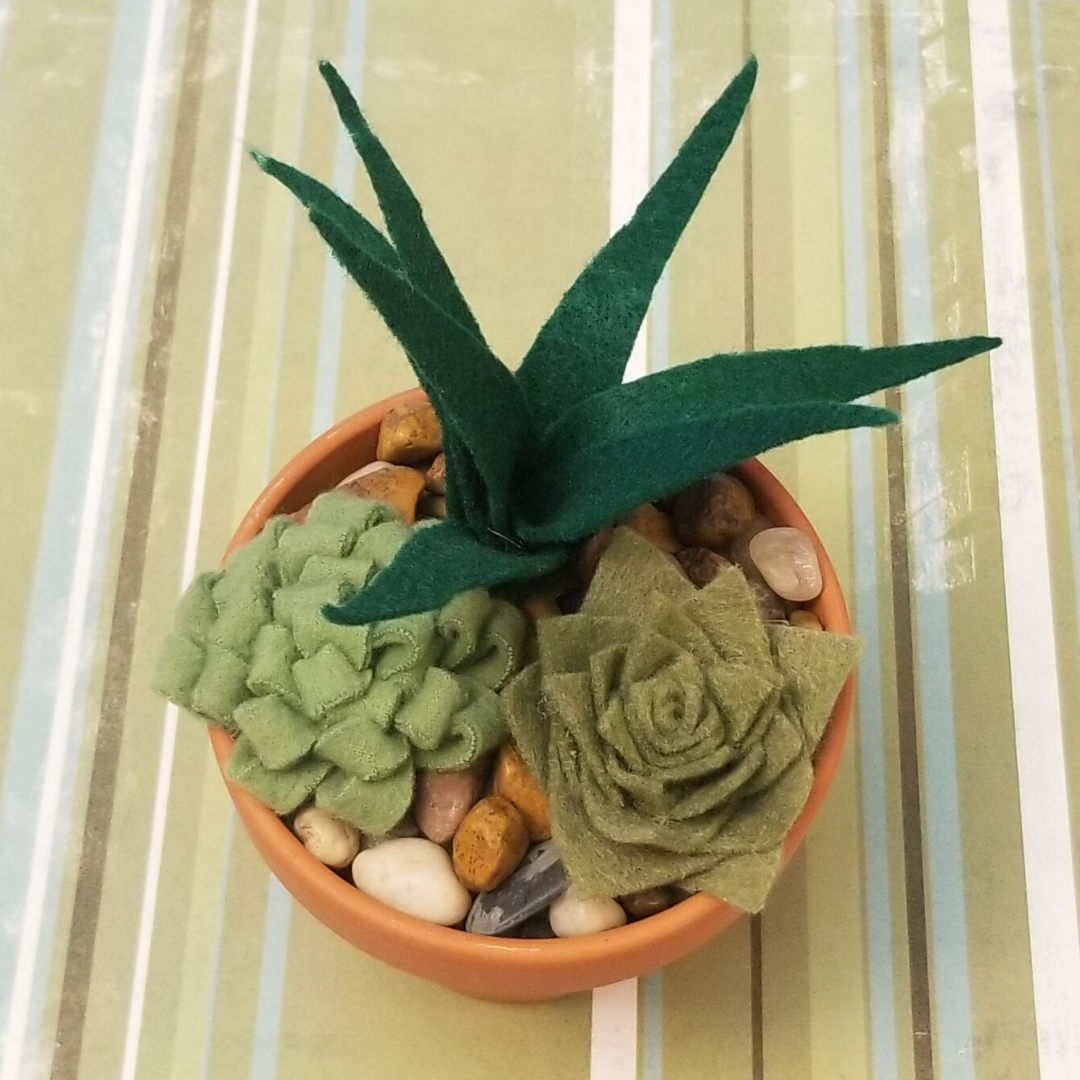 Fabric and felt succulents in a small pot, featuring a tall aloe like one and shorter, round succulents