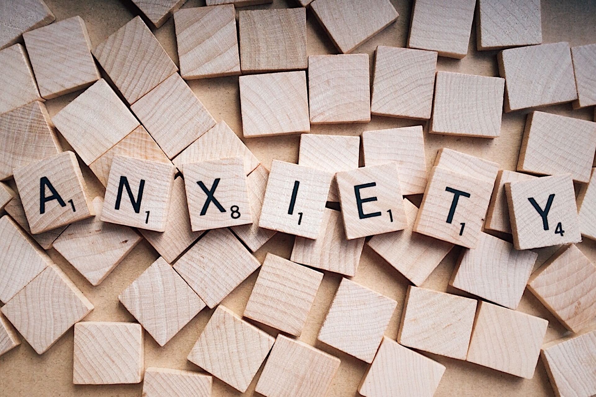 The word "anxiety" is spelled with scrabble tiles over a background of overturned scrabble tiles.