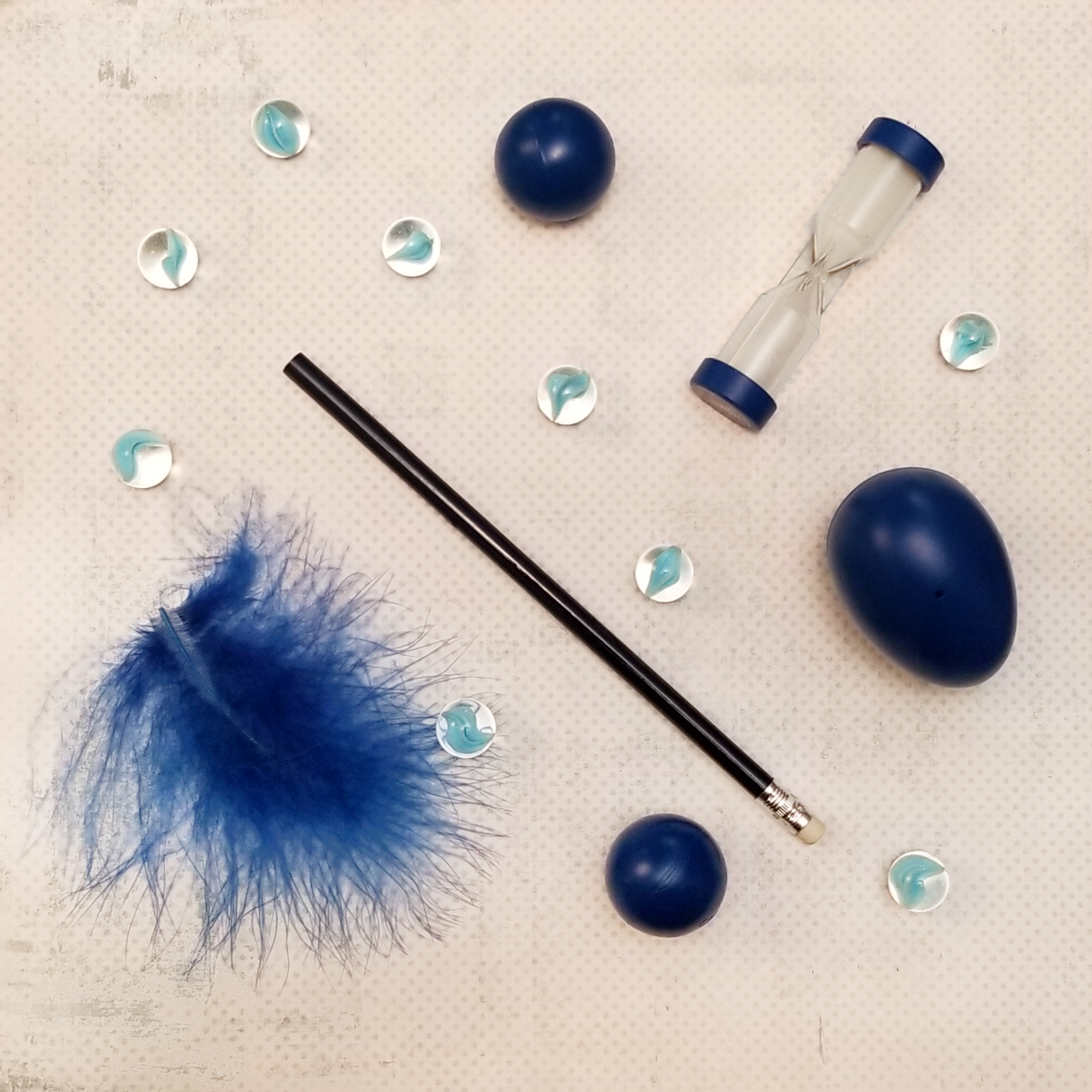 An image of various game props for Minute to Win It games, including a feather, marbles, a pencil, plastic egg, and minute timer.