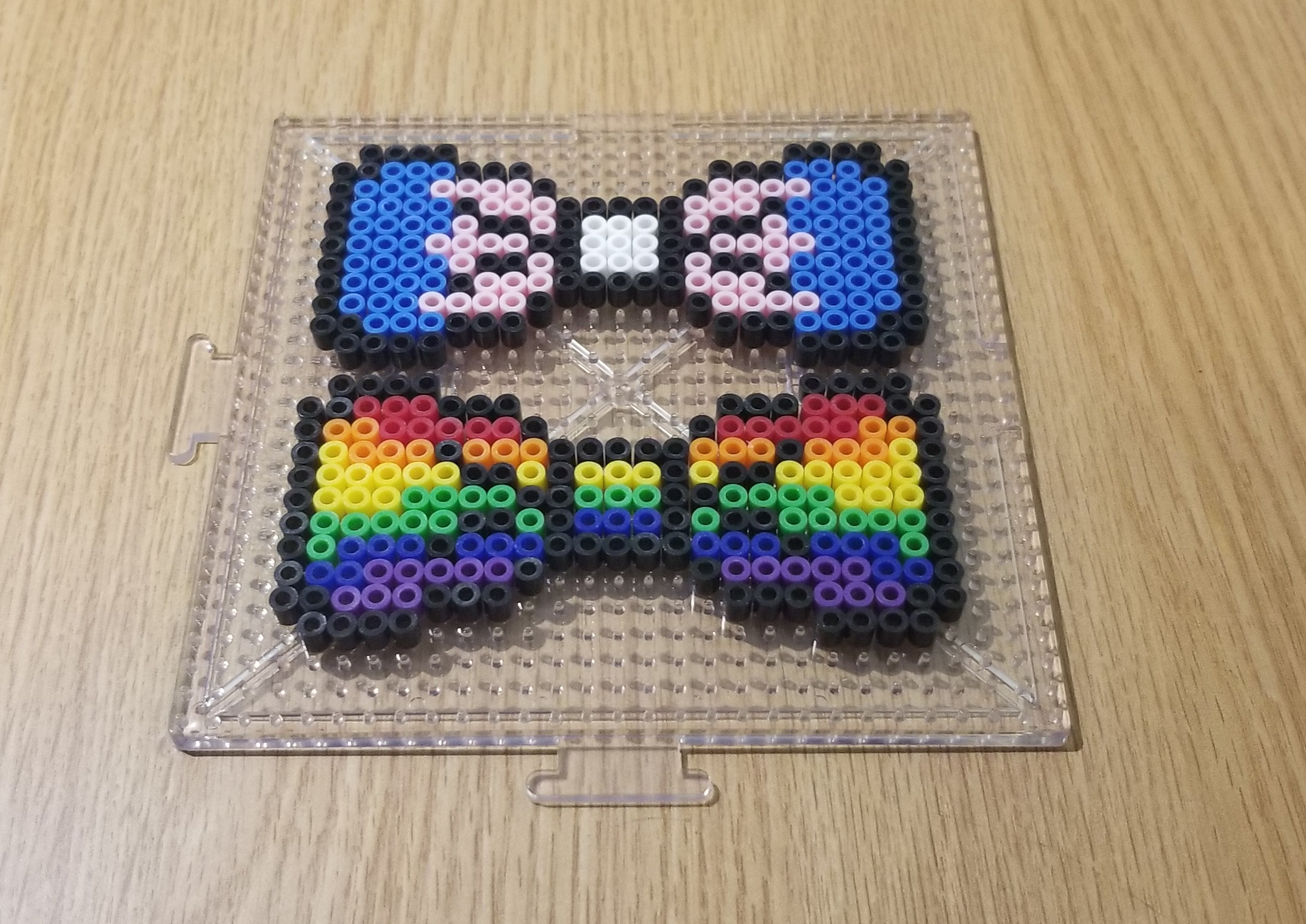 A sample of a rainbow bow tie and a trans pride colored bow tie, both made out of perler beads.