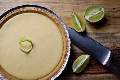 A key lime pie with a graham cracker crust, light yellow-green filling, and lime garnishes