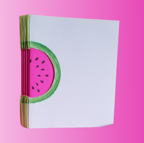 A small, square notebook with a white cover and cut out watermelon shape on its spine