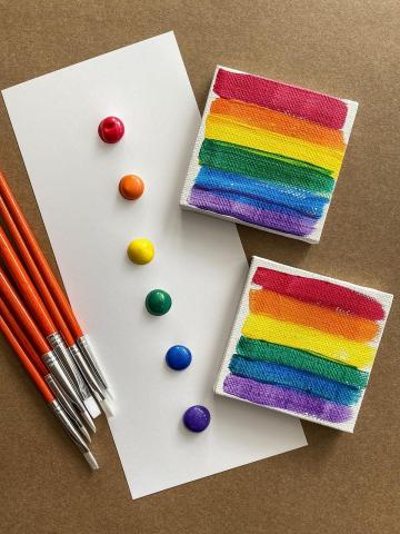 Two tiny rainbow paintings alongside a piece of paper with paint dots and brushes