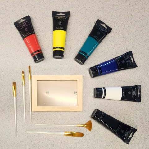 A plain picture frame arranged with paint brushes and tubes of acrylic paint