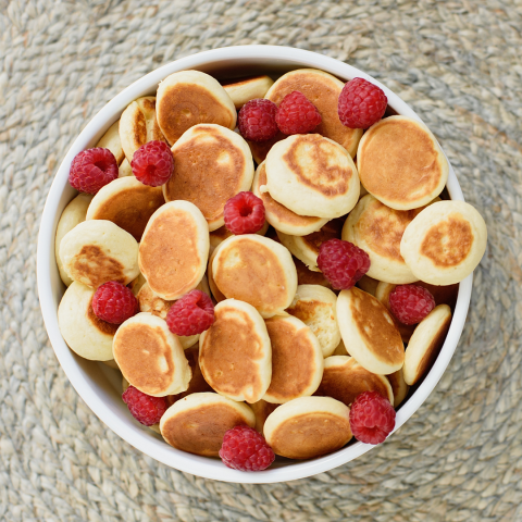 A bowl full of tiny, 1 inch pancakes and raspberries
