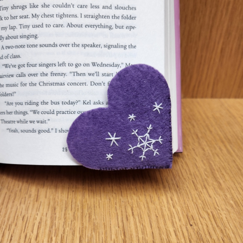 A sample of the craft: a purple felt heart on the corner of a book; it is embroidered with simple snowflakes.