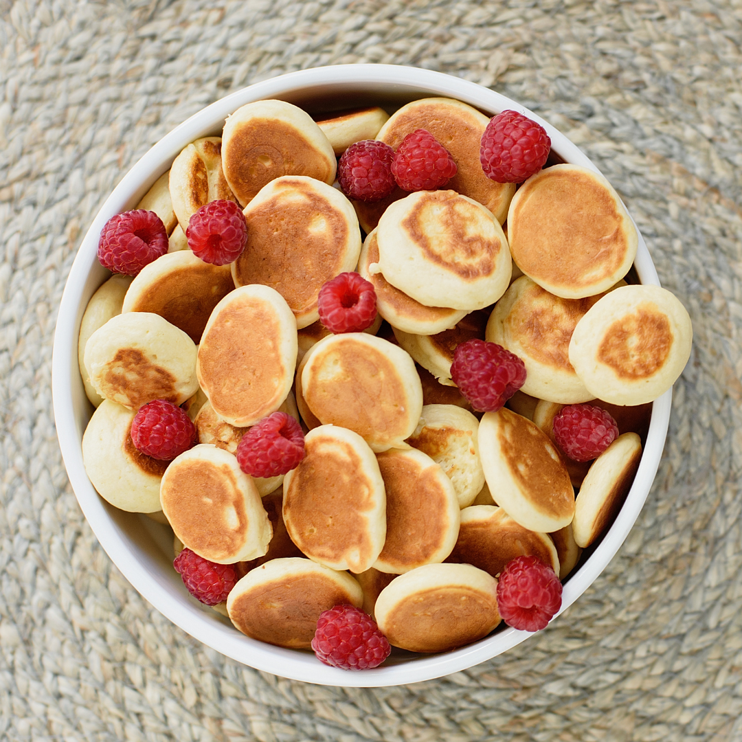 A bowl full of tiny, 1 inch pancakes and raspberries
