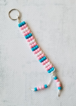 A keychain with blue, pink, and white pony beads arranged in stripes to mimic the transgender pride flag.