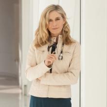 A picture of Delaney Ruston, a middle aged white woman with wavy blonde hair in a tan coat with a stethoscope.